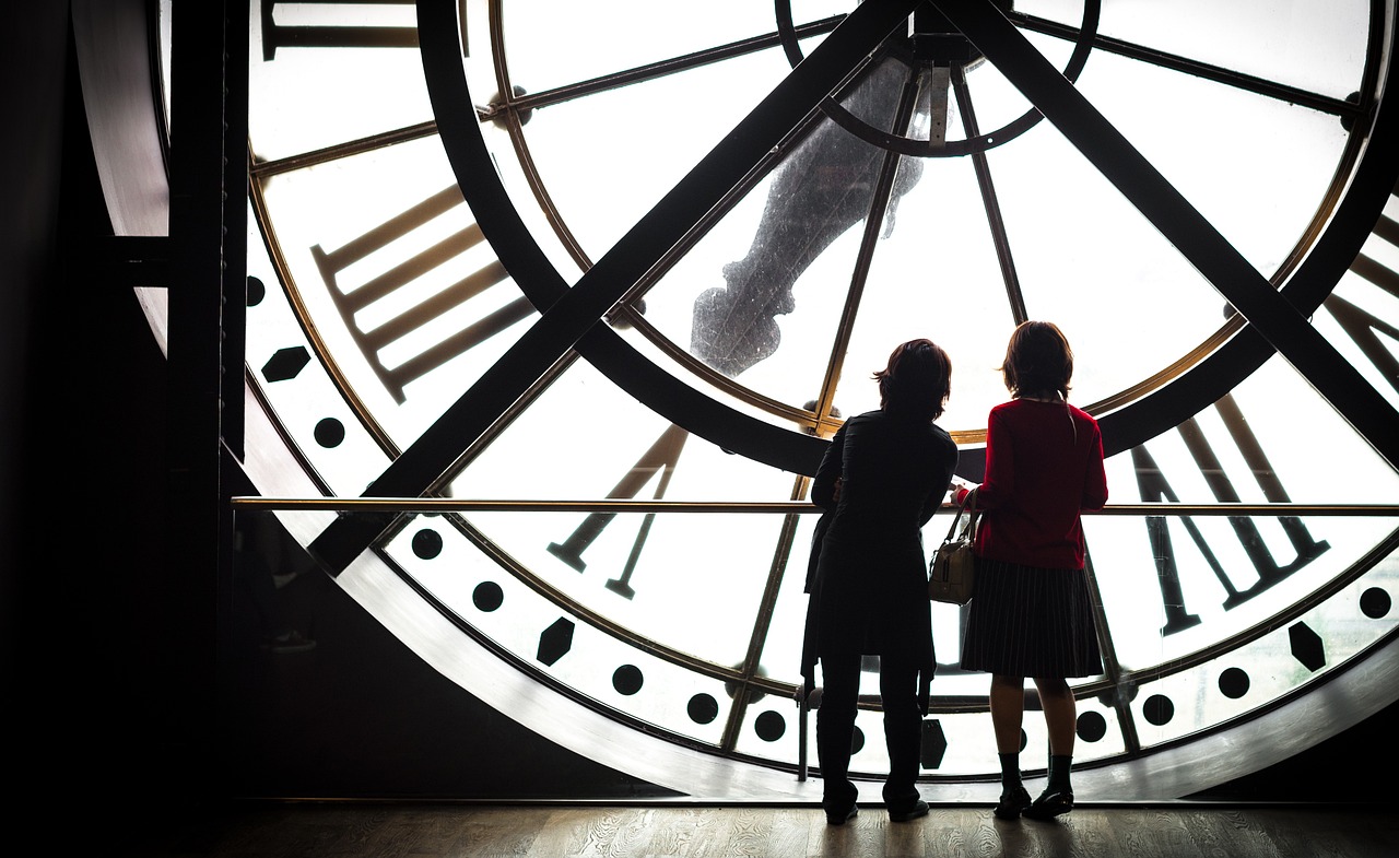 Two people watching a clock, visualize how in software project management adding more people to a late project makes it later.